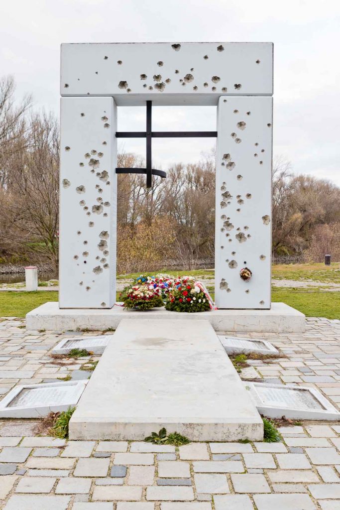 Wite gate-shaped monument with bullet holds and bent iron bars